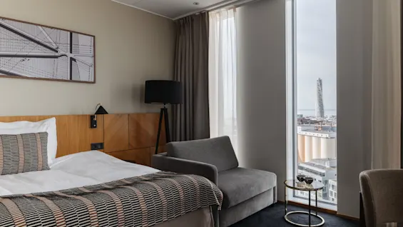 Et moderne hotellrom med en komfortabel seng, en koselig lenestol og et stort vindu med utsikt over byen.
