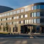 En moderne, fleretasjes bygning merket "Skiper Hotel" står ved en gate og reflekterer sollys. Bygningen har store vinduer og steinfasade i kupert terreng.