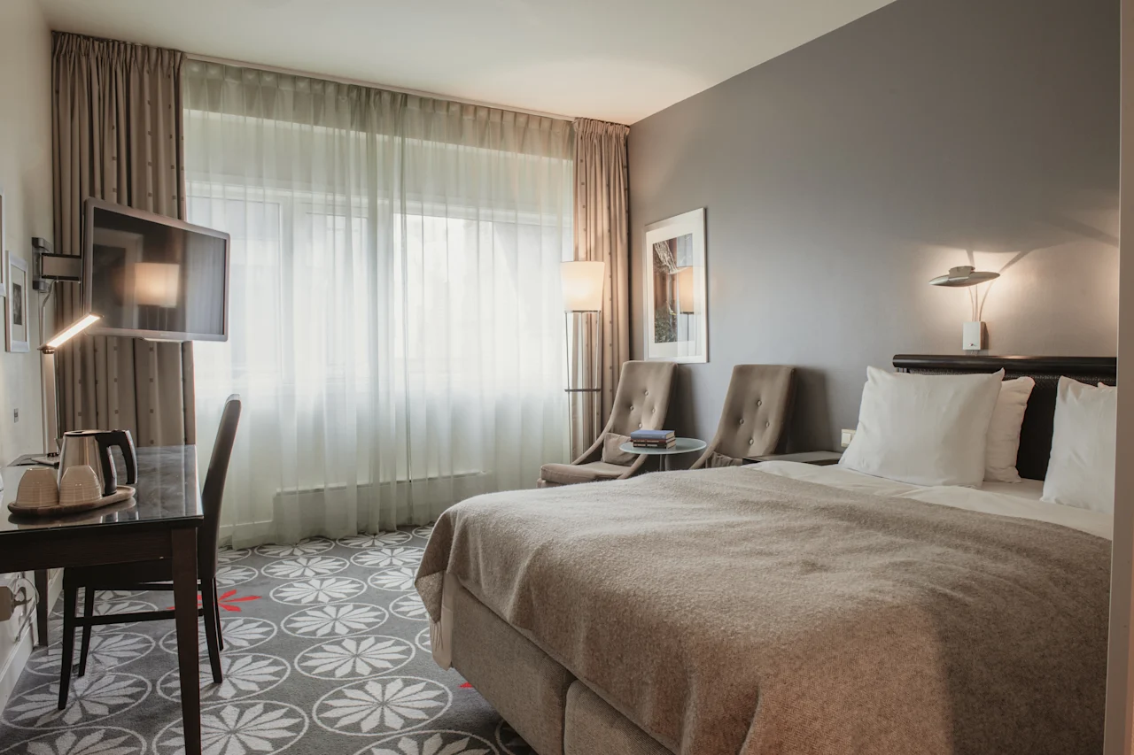 Ett mysigt hotellrum med en bekväm säng, en skrivbordshörna och en sittgrupp vid ett stort fönster.