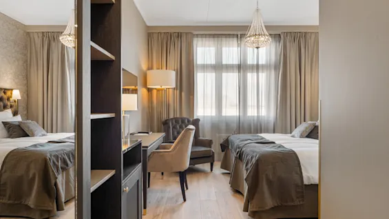 Et rummeligt og elegant indrettet hotelværelse med to komfortable senge, et funktionelt skrivebordsområde og varm, indbydende belysning.