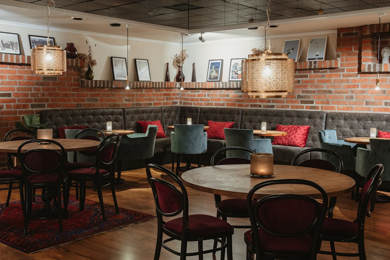 En varm och inbjudande restaurang- eller barinteriör med tegelväggar, plyschmöbler, träbord och stämningsfull belysning.