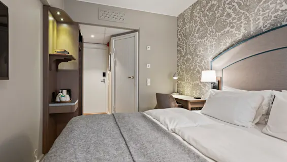 A cozy hotel room with a comfortable bed, a desk for work, and a refreshment station, inviting guests to relax.