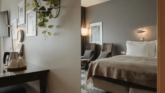 Ett mysigt hotellrum med en bekväm säng, två fåtöljer och ett litet bord med vattenkokare, för en avkopplande vistelse.