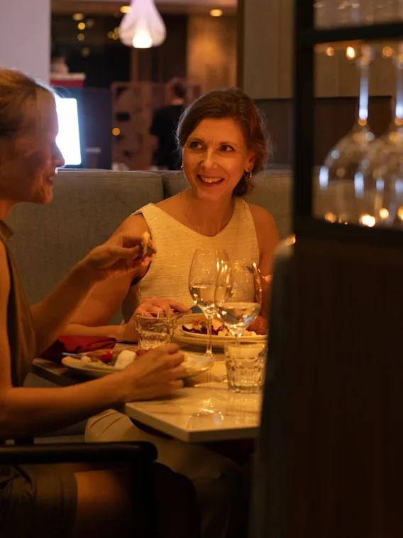 Two guests enjoying a meal and conversation at a restaurant, with drinks and food on the table in a warm, inviting atmosphere.