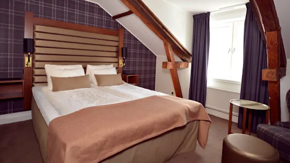 A neatly made double bed in a cozy room with exposed wooden beams and tartan patterns on the walls.