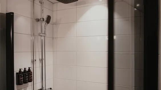Puhdas, moderni suihkutila valkoisilla laatoilla, varustettuna sade- ja käsisuihkulla, valmiina virkistävään pesuun.
