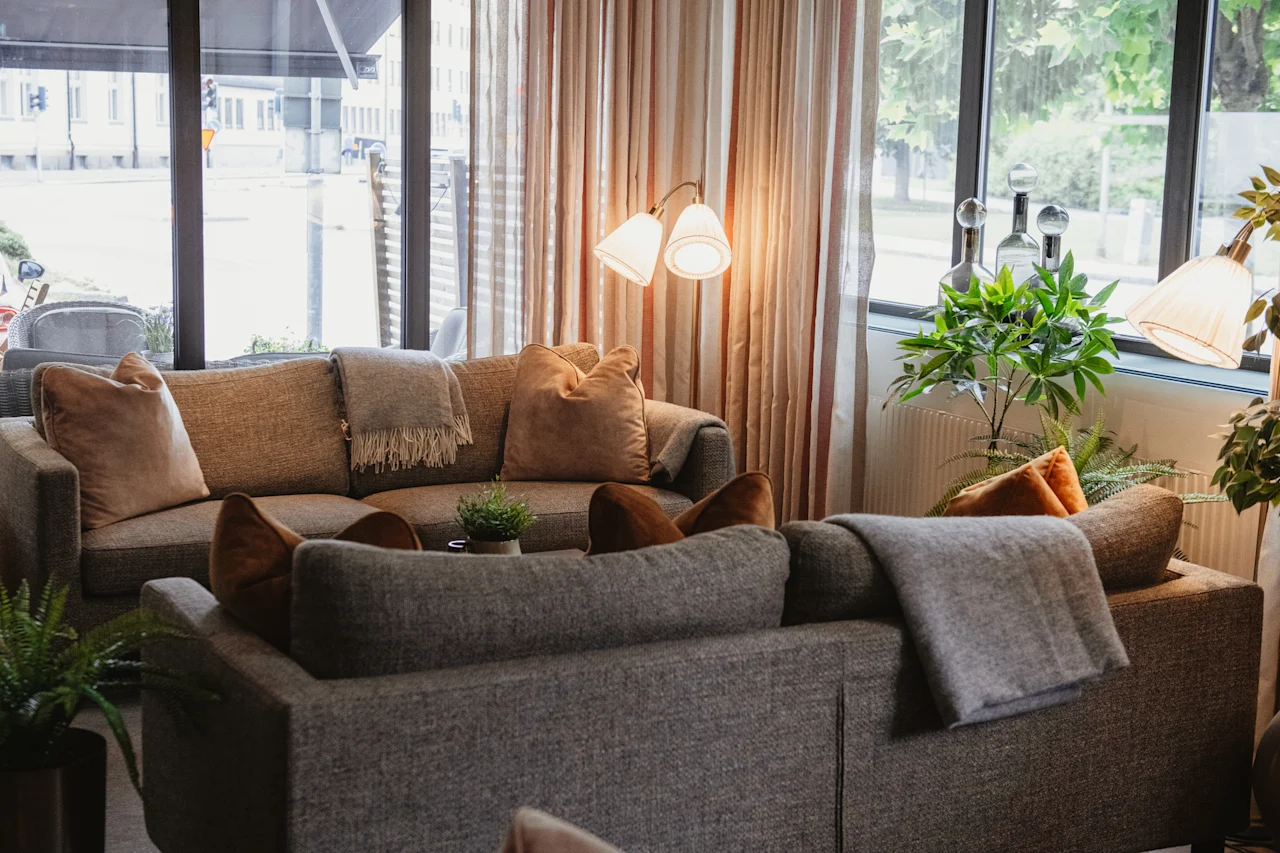 A cozy lounge area with comfortable sofas, warm blankets, and soft lighting, looking out onto a street.