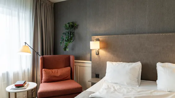 A comfortable and inviting hotel room at Home Hotel Grand Bodø, featuring a bed, a cozy reading nook with a chair, and soft lighting.