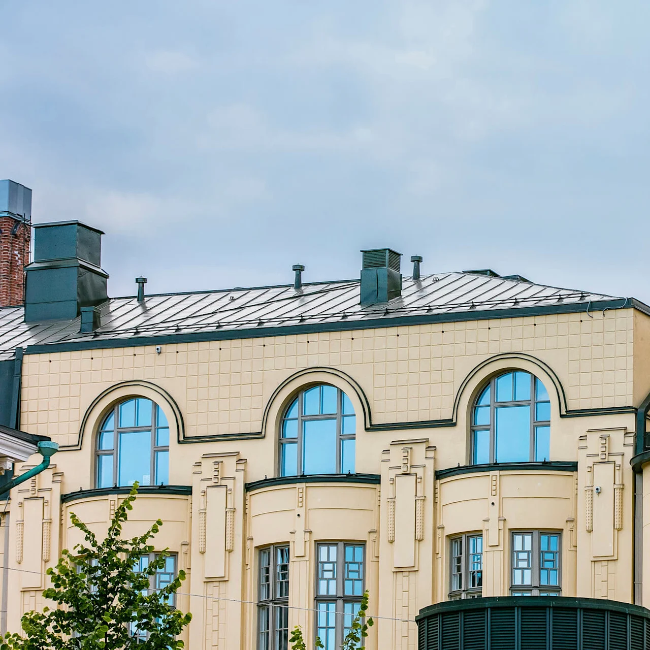 En beige bygning med buede vinduer og et metalltak, med teksten "HOTEL L ROBERTS" på hjørnet, under en overskyet himmel.