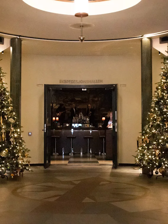 En festlig hotellobby med to store, opplyste juletrær og trapper med girlandere som fører til et barområde.