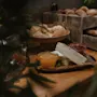 Ostar och pålägg är upplagda på en träbricka bredvid olika brödbullar i rustika trälådor, på ett träbord, omgivna av gröna växter.