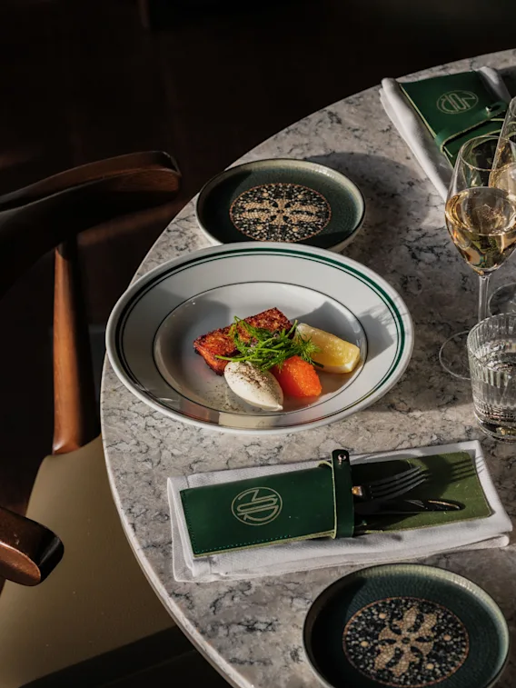 Kauniisti katettu marmoripöytä, jossa on gourmet-annos, viinilaseja ja tyylikäs kattaus lämpimässä auringonvalossa.