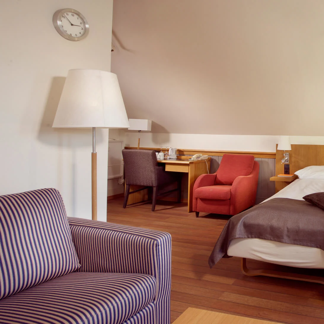Et pænt arrangeret hotelværelse med to enkeltsenge, møbler og varmt lys.