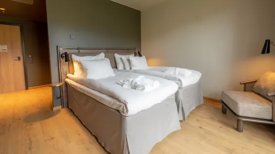Ett prydligt hotellrum med två enkelsängar bredvid varandra, bäddade med vita lakan; en enkel och avslappnande atmosfär med neutrala färger.