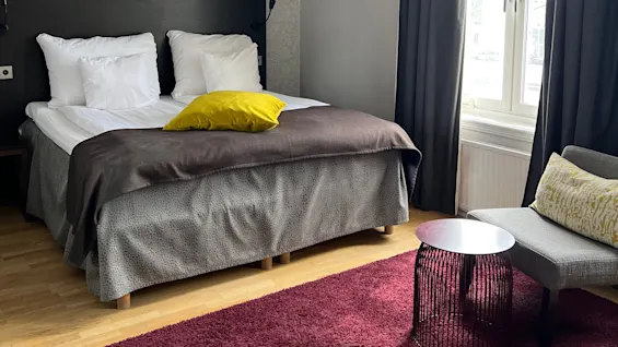A neatly arranged bedroom with a bed, patterned wallpaper, and a large pendant lamp. The room has a cozy and modern aesthetic.