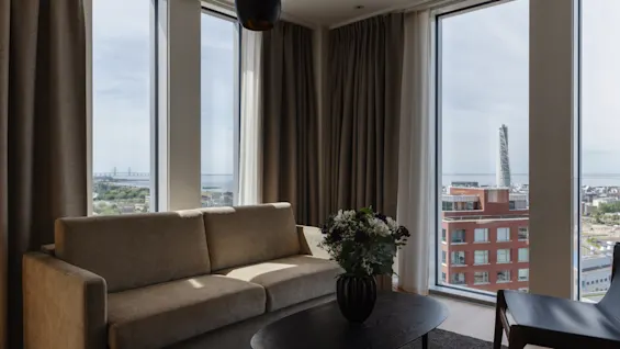 Moderne stue med sofa, salongbord og store vinduer med utsikt over by og sjø.