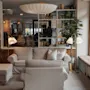A cozy hotel lounge with comfortable sofas, a large bookshelf, and a window seat, creating a welcoming atmosphere. Visible text: HOTEL