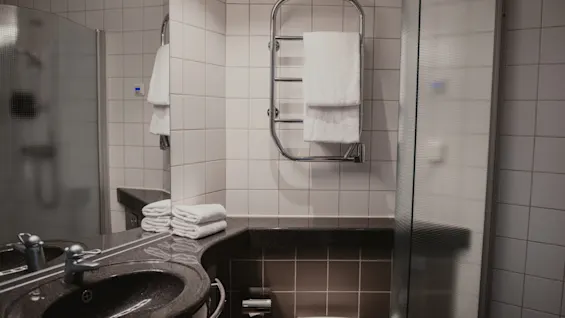 A clean and modern hotel bathroom at Home Hotel Uppsala, featuring a sink, toilet, shower, and fresh white towels on a heated rack.