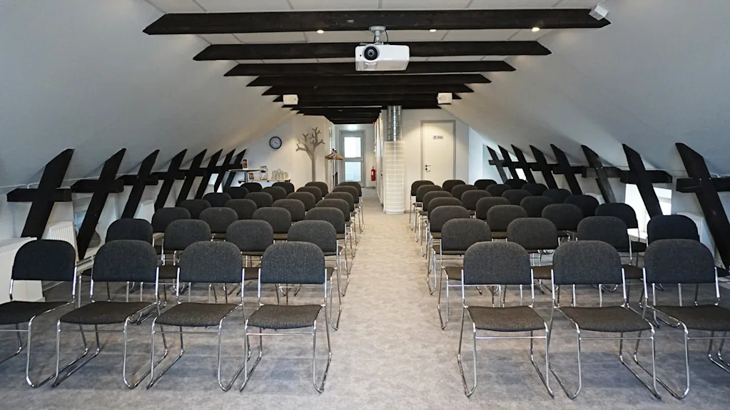 Ett modernt konferensrum med rader av stolar, en projektor och synliga takbjälkar, redo för en presentation.