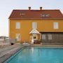 En livlig gul byggnad med rött tak vetter mot en uppfriskande utomhuspool med solstolar en solig dag.