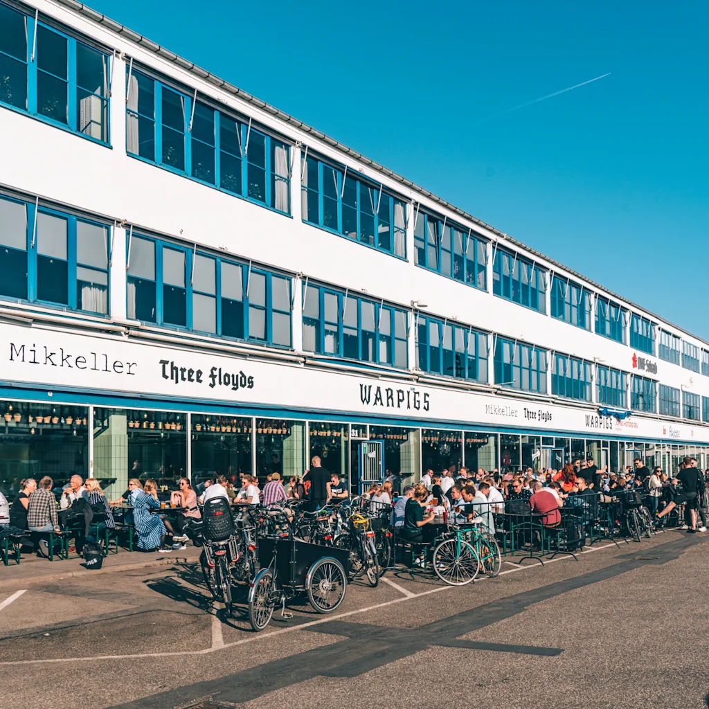 People enjoying outdoor dining and drinks at a row of lively establishments in Kødbyen, Copenhagen’s Meatpacking District, with bicycles parked.