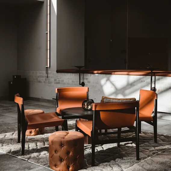 En mysig lounge på Quality Hotel Arlanda XPO med orange stolar och puffar runt ett bord på en matta, badad i solljus.