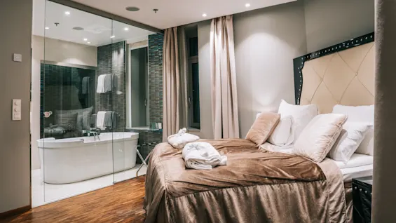 Ett lyxigt hotellrum med en stor säng och ett öppet badrum med ett fristående badkar.