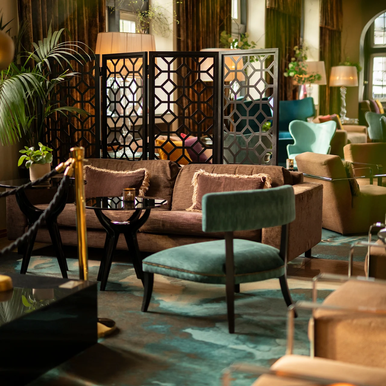 A cozy lounge area features elegant seating, a decorative partition, and soft lighting, surrounded by plush chairs and plants, creating a warm and inviting atmosphere.