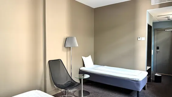 Ett mysigt hotellrum med två enkelsängar, en modern stol och en golvlampa, som erbjuder en bekväm vistelse.