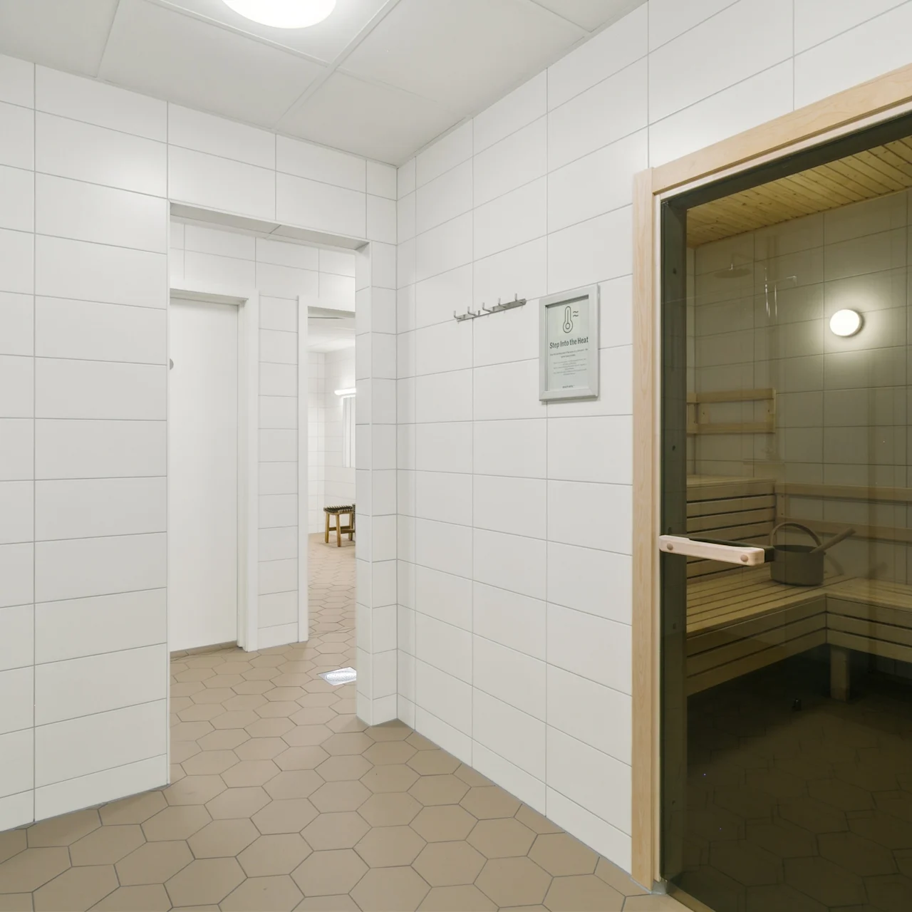 Et træbadstue, set gennem en glasdør, i en flisebelagt gang. Teksten lyder "Nautilus Condominiums." Sekskantede fliser strækker sig gennem et godt oplyst miljø.