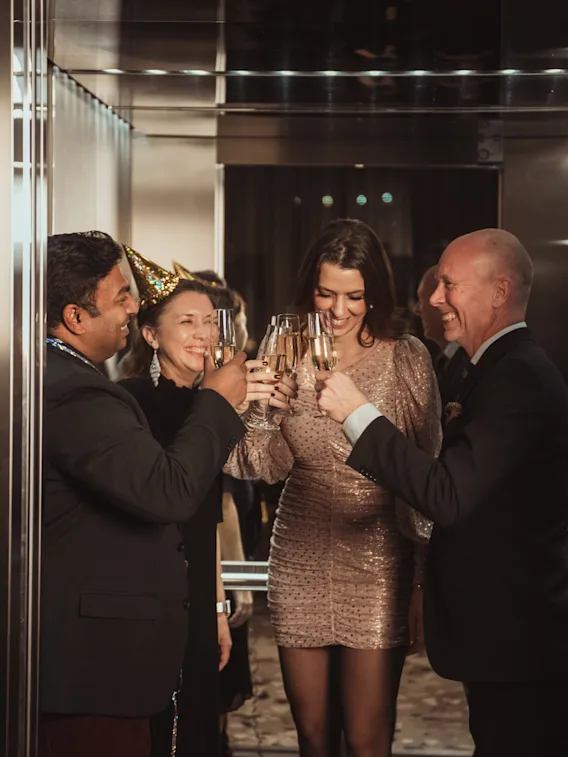 En gruppe glade mennesker skåler med champagneglass og feirer en spesiell anledning. En person har på seg en festhatt.