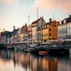 Colorful houses and old wooden boats reflecting in the water at Copenhagen Nyhavn during a beautiful sunset.