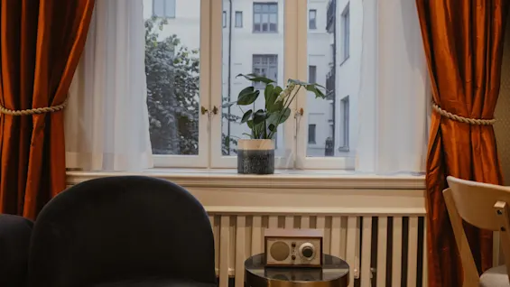 Et hyggeligt værelse på Home Hotel Wellington med vinduesudsigt, en plante i vindueskarmen, en behagelig stol og en vintage radio.