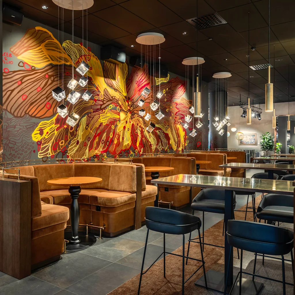 A modern and inviting restaurant interior with comfortable booth seating, high tables, and a vibrant abstract mural on the wall.