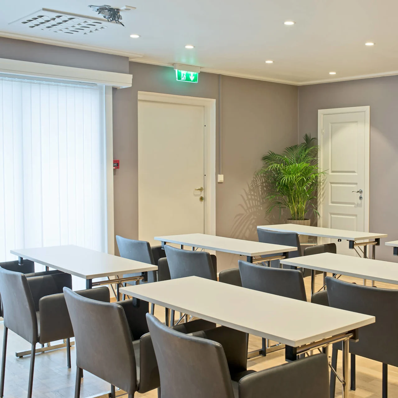 Et tomt møterom med bord, stoler, og en stor skjerm på veggen. Moderne, godt opplyst, klart for konferanse eller presentasjon.