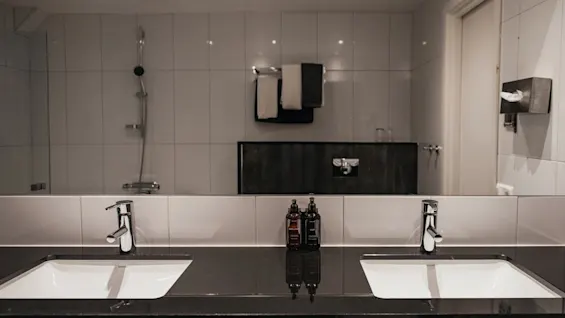 Ett välutrustat hotellbadrum med dubbla handfat, prydligt placerade toalettartiklar, som speglar ett duschutrymme och fräscha handdukar.