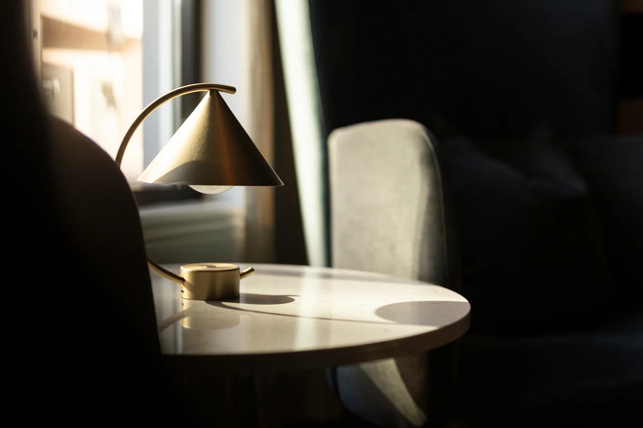 A warm, sunlit indoor scene with a stylish lamp on a table next to a comfortable chair, creating a cozy atmosphere.