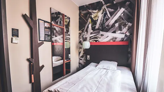 En ryddig seng i et hotellrom med moderne innredning og tapet med strimler av trykt materiale.