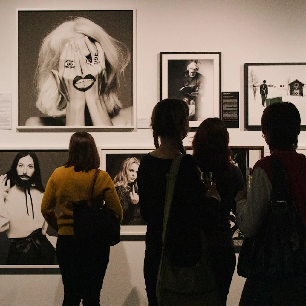 Människor betraktar en samling svartvita fotografier utställda på en vägg i ett konstgalleri.