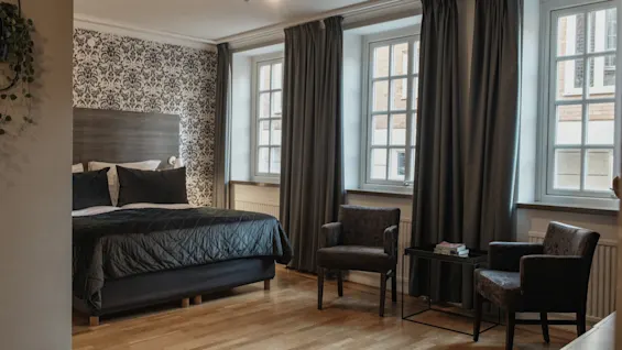 Ett välkomnande hotellrum på Home Hotel Grand, Helsingborg, med en bekväm säng och en mysig sittgrupp vid fönstren.