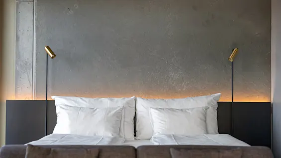 Deluxe rom på Comfort Hotel Porsgrunn. En koselig seng med hvitt sengetøy, en mørk sengegavl og varm belysning på en teksturert vegg.