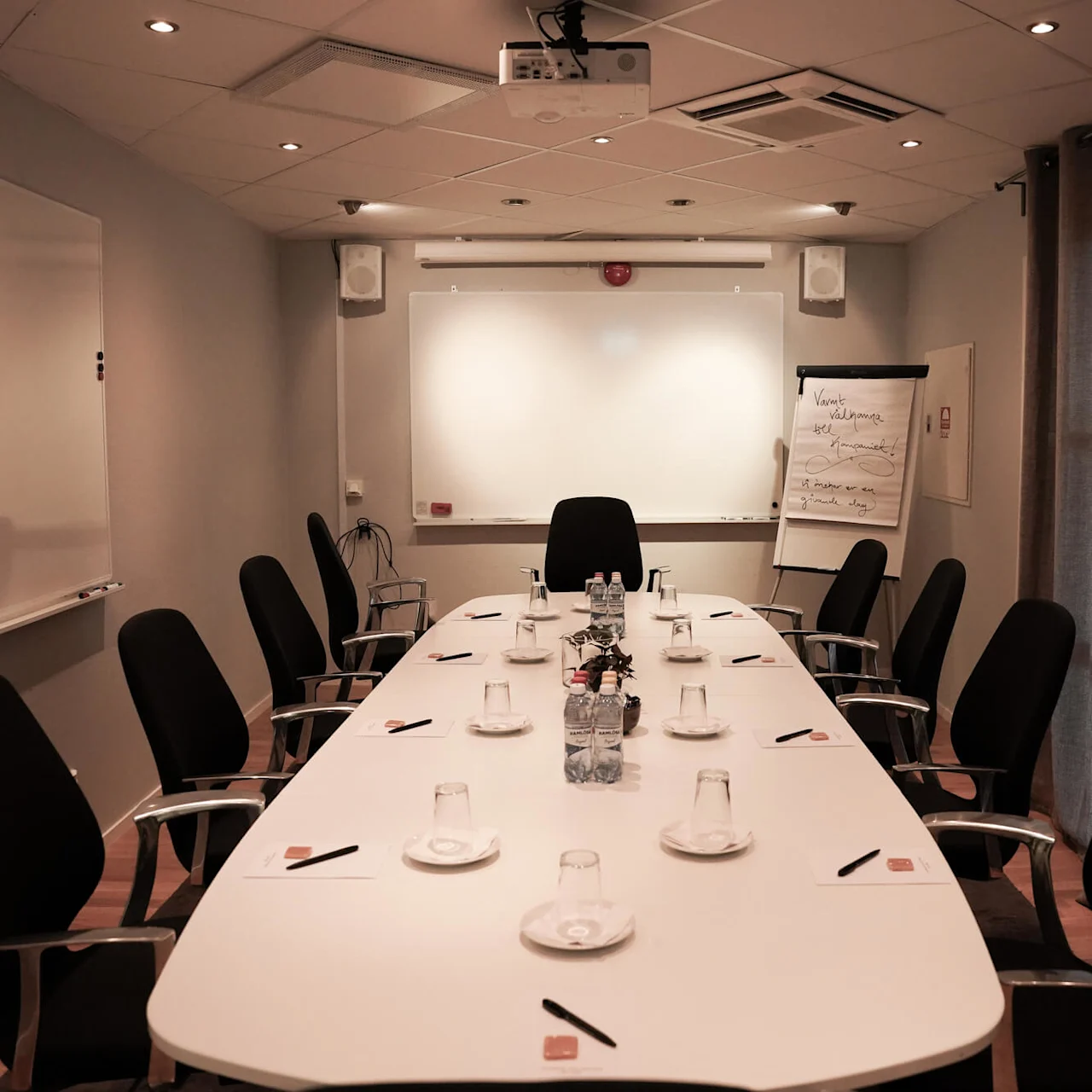 A conference room with a long table, chairs, and presentation equipment, ready for a meeting.