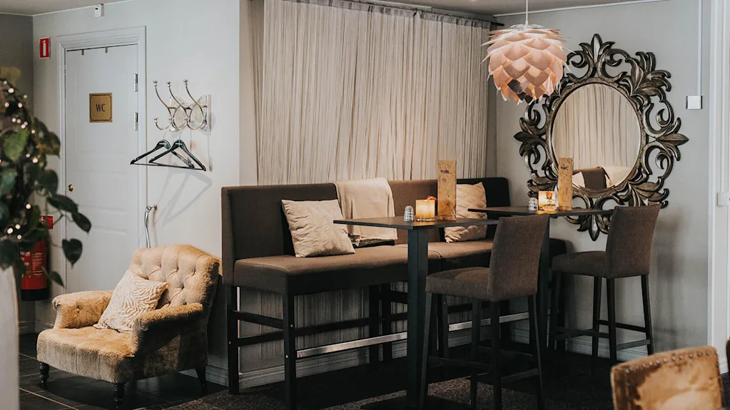 En elegant innredning med koselige sitteplasser, lys fra stearinlys og et dekorativt speil; antyder et avslappet spise- eller venteområde.