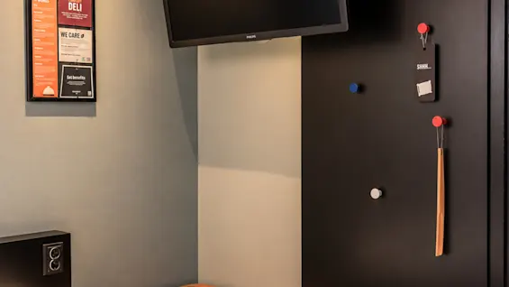 Modern hotel room corner featuring a bed, wall-mounted TV, and a black clothes rack panel.