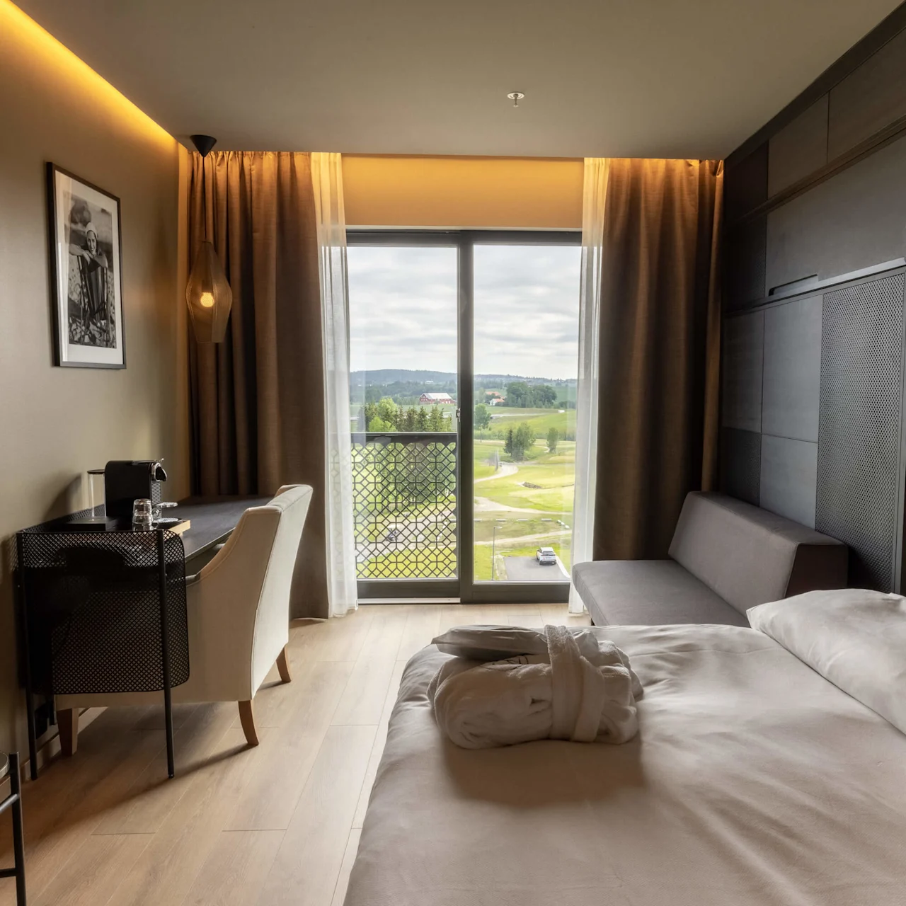 Ett modernt hotellrum med en snyggt bäddad säng, stilfulla möbler, och ett stort fönster som visar en naturskön utomhusutsikt.