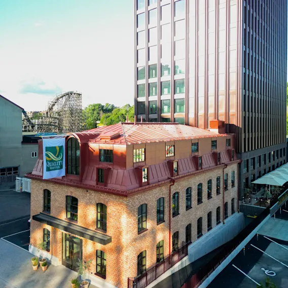 A historic brick building with a red roof stands next to a modern high-rise hotel tower under a clear blue sky.