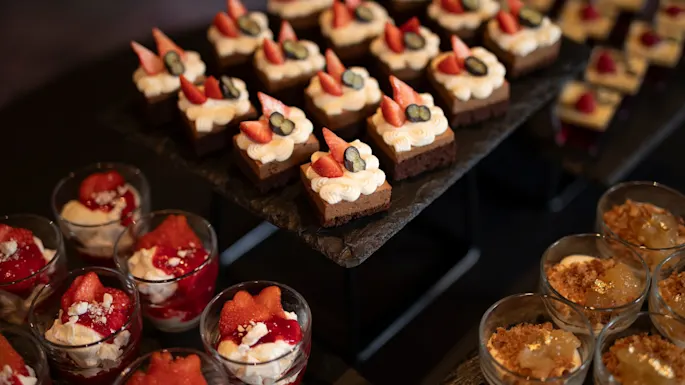 A delightful spread of various desserts, including small cakes topped with berries and creamy parfaits in glasses.