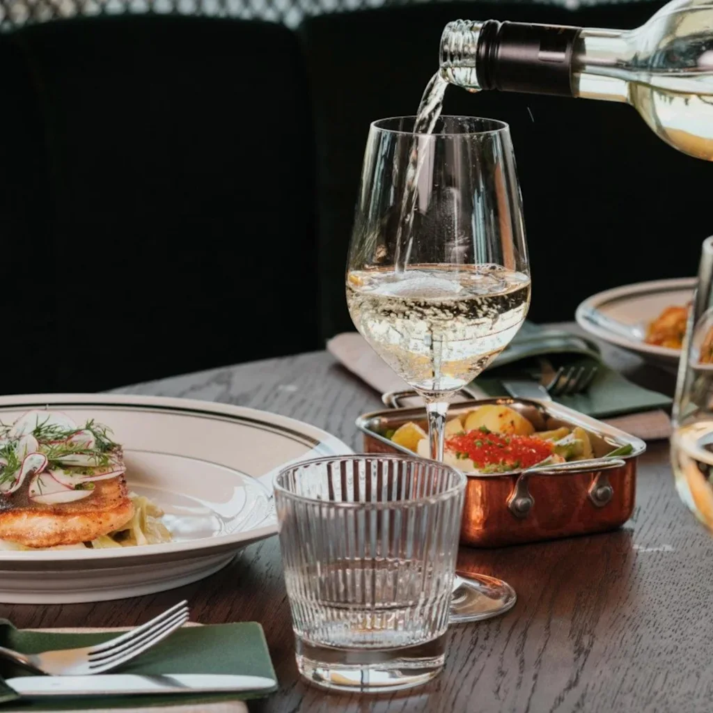 NÒR Helsinki Airport. Hvitvin helles i et glass ved et restaurantbord med et deilig måltid.