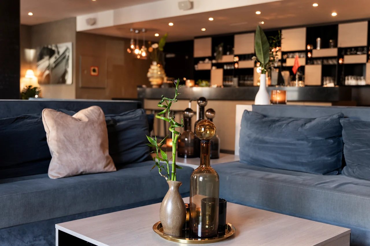 En hyggelig hotellounge med bløde blå sofaer, et sofabord prydet med bambus og glasflasker, og en smart bar.