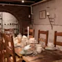 Et rustikt bord er dækket med tallerkener, glas og et tændt lys i et hyggeligt kælderrum med murstensbuer og vægdekorationer.